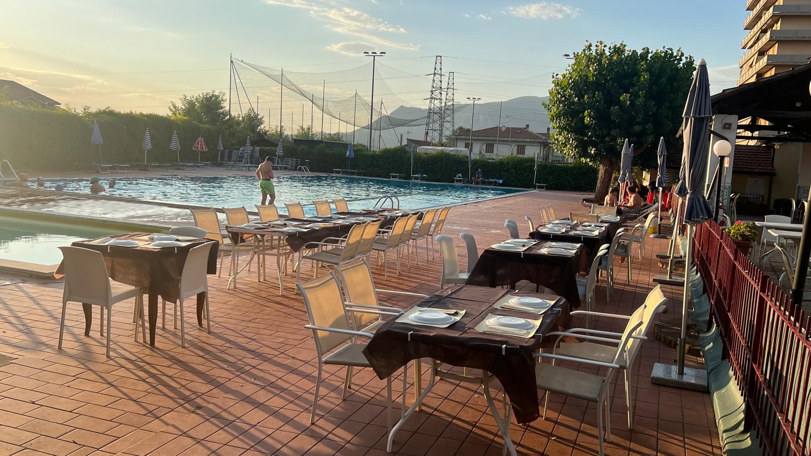 Tavoli con tovaglie marroni e sedie bianche sulla terrazza in cotto a bordo piscina del Ristò Sporting al tramonto